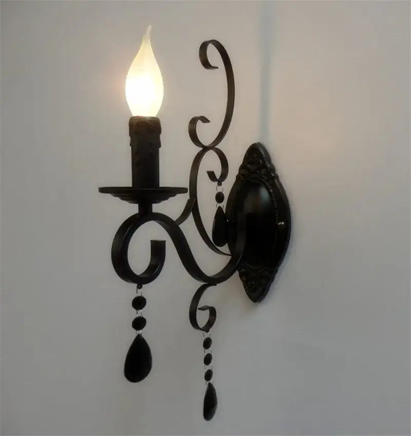Ornate black wrought iron wall lamp with scrollwork and teardrop crystals featuring a candle-style bulb for living room decorbites black wrought design