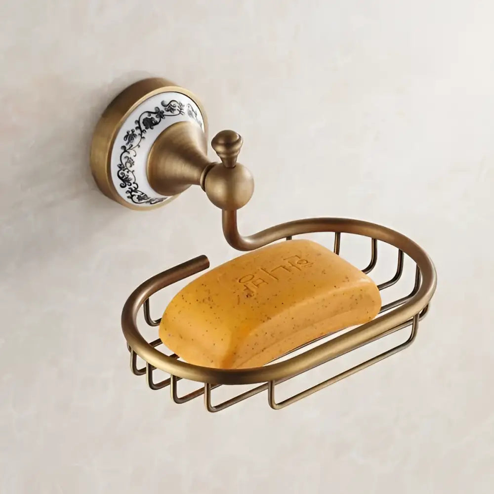 Antique brass soap dish with decorative white ceramic backplate and oval wire basket holding yellow soap in bath hardware set