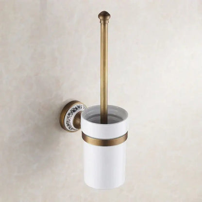 Antique brass-finished toilet brush holder with white ceramic cup and black floral mounting plate in bath hardware set