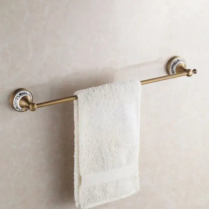 Antique brass towel rack with decorative white ceramic end caps holding a terry cloth towel in bath hardware set