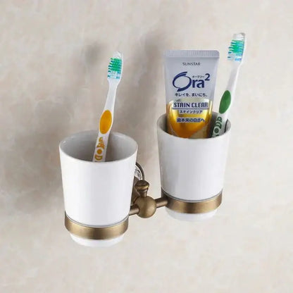 Ornate brass and white ceramic bath hardware set featuring a dual cup toothbrush holder with gold toned accents
