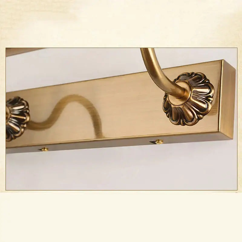 Brass-finished ornate bathroom mirror lamp with decorative scrollwork and flower-like end caps for elegant lighting