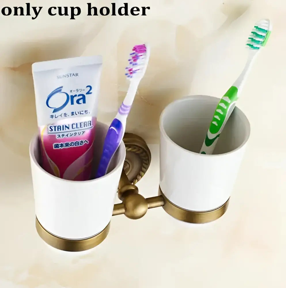 White ceramic cup holder with gold-toned copper bracket holding toothbrushes in ornate decorbites copper bathroom set