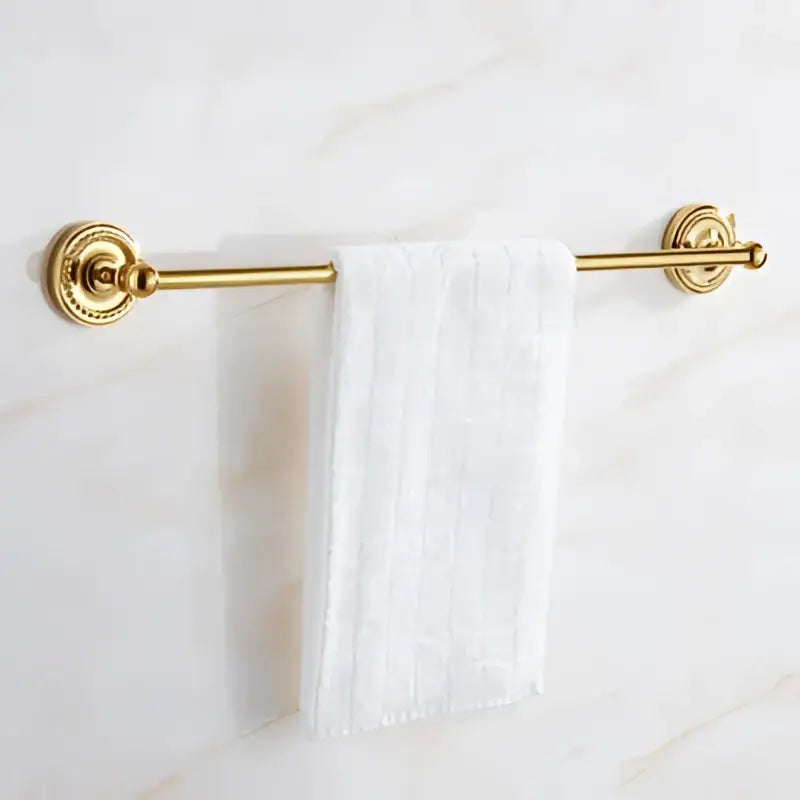Gold-toned brass towel rack with ornate circular end caps holding white textured towel in brass gold bathroom set decorbites brass gold