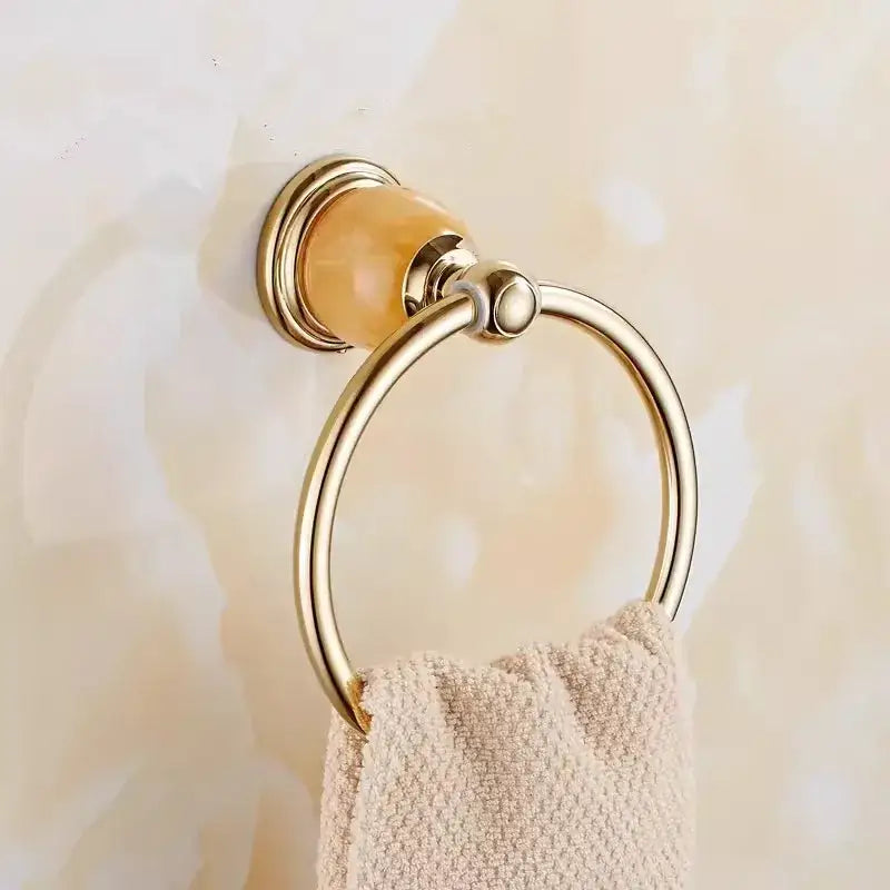 Gold-toned towel ring with polished brass finish and amber ceramic accent holding beige towel from brass jade bathroom set