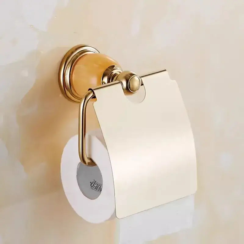 Gold-toned toilet paper holder with polished metallic finish and amber ceramic base in brass jade bathroom set by decorbites