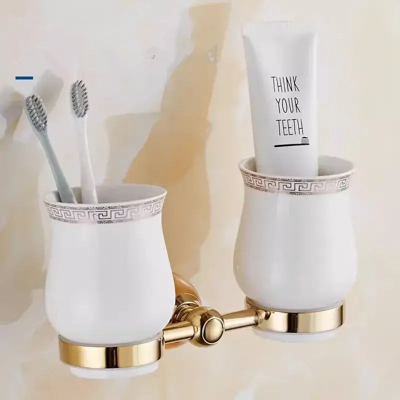 White ceramic toothbrush holder with gold greek key rim holding two toothbrushes in ornate brass jade bathroom set