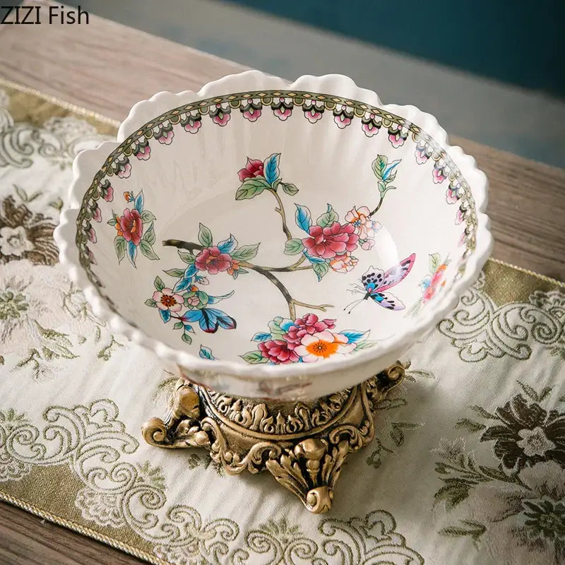 A delicate white porcelain pattern fruit bowl with colorful flower pattern and butterfly designs on a gold stand
