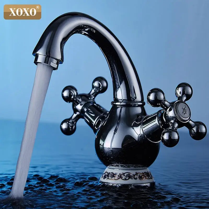 Ornate gold and chrome double handle chrome basin faucet with curved spout and cross-handle knobs on white ceramic base