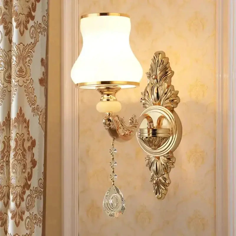 Ornate gold-toned crystal wall sconce with frosted glass shade and dangling teardrop pendant for elegant bedroom decor