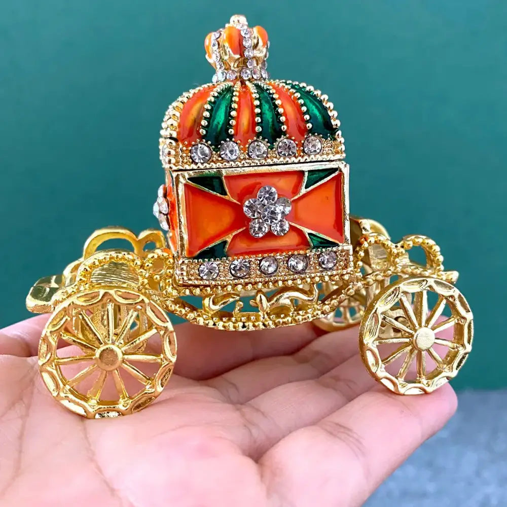 Ornate gold enamel crown jewelry box shaped like a carriage with orange green accents and rhinestone details