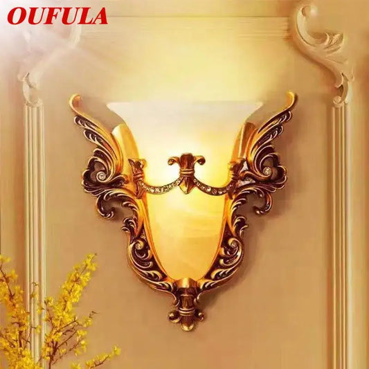 Ornate gold glass sconce light with warm amber shade, crystal accents, and intricate scrollwork wall lamp for living room