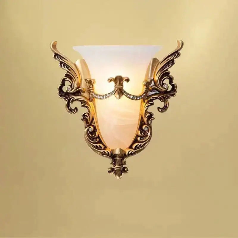 Ornate gold-toned glass sconce light with intricate scrollwork and frosted shade for elegant living room wall lamp
