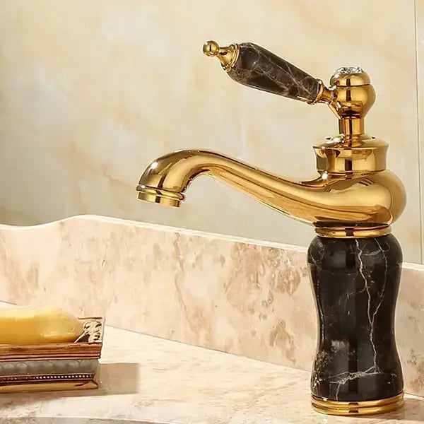 Ornate gold bathroom basin sink faucet with black marble handle and base featuring elegant curves and detailing