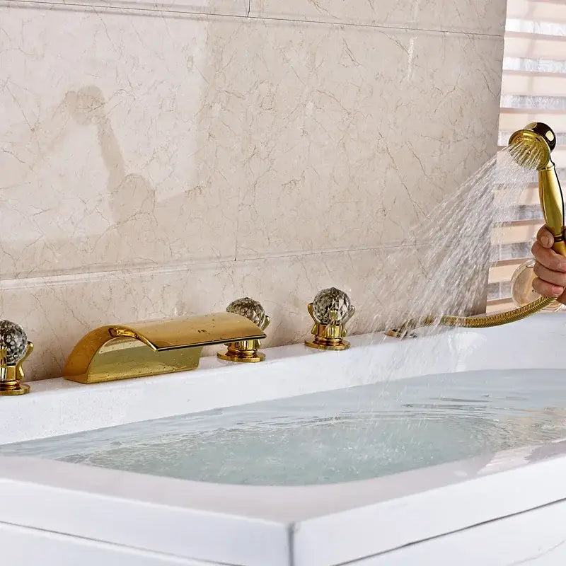 Ornate gold-toned bath tub faucet with crystal knobs and sleek modern design featuring a led waterfall and handshower