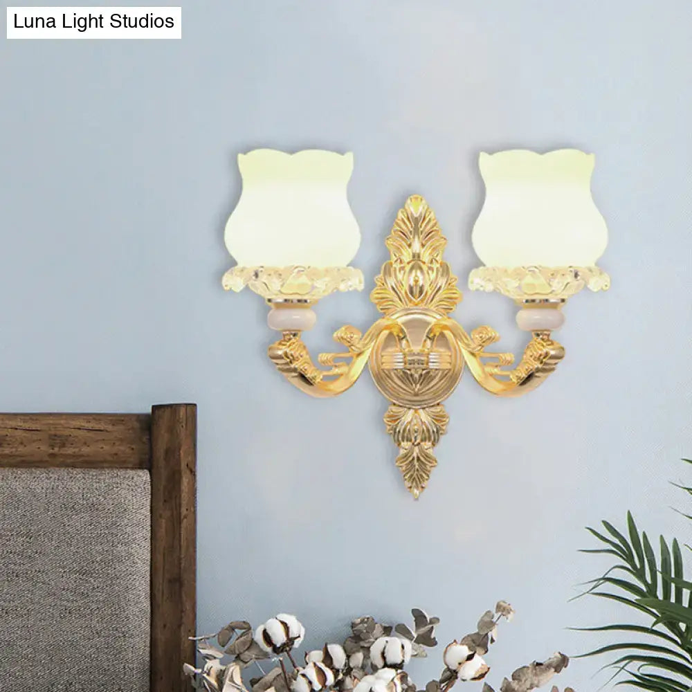 Ornate gold wall light with two frosted glass bloom shades and fixture width suitable for living room use