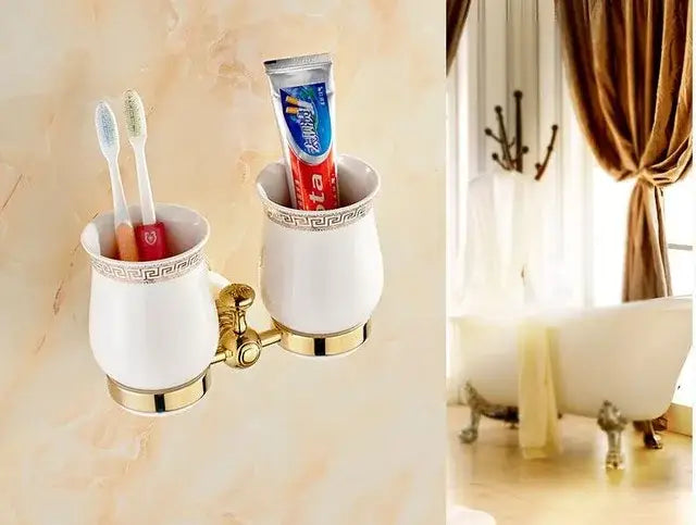 White ceramic toothbrush holder with gold trim and greek key pattern holding two toothbrushes in brass jade bathroom hardware set by decorbites