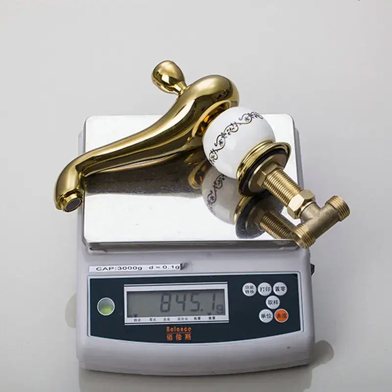 Gold finished bathroom faucet set with white porcelain knob featuring black ornate detailing for elegant bathroom use