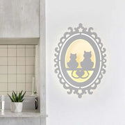 Elegant gray ornate wall light fixture with two cat silhouettes seated on heart-shaped ledge illuminated warm yellow light