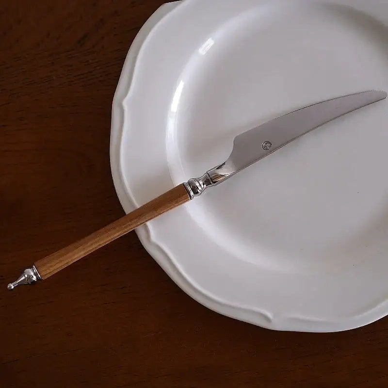 A sleek silver-bladed cheese knife with wooden handle and metal accents from an ornate stainless steel tableware set
