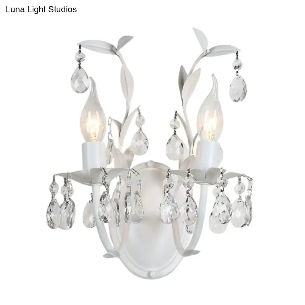White ornate wall light fixture with silver crystal teardrop pendants and leaf-shaped metal arms for bedroom use