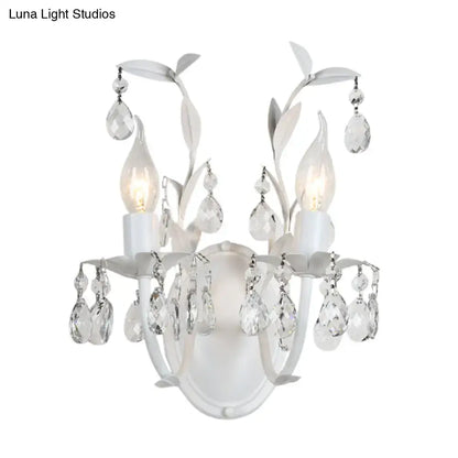 White ornate wall light fixture with silver crystal teardrop pendants and leaf-shaped metal arms for bedroom use