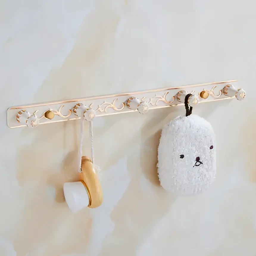 Ornate white and gold decorbites bath hardware set with wall-mounted towel rack holding plush bunny loofah and wooden brush