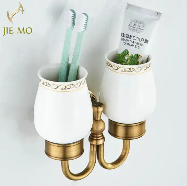 Ornate white ceramic double cup holder with gold detailing and brass base holding two mint green toothbrushes