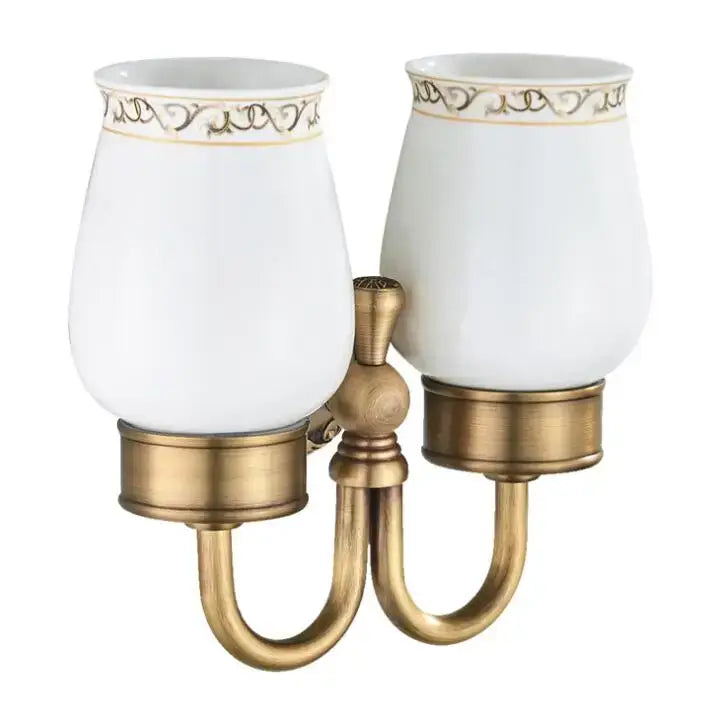 Antique brass two-light bathroom sconce with white ceramic shades and gold filigree detailing double cup holder