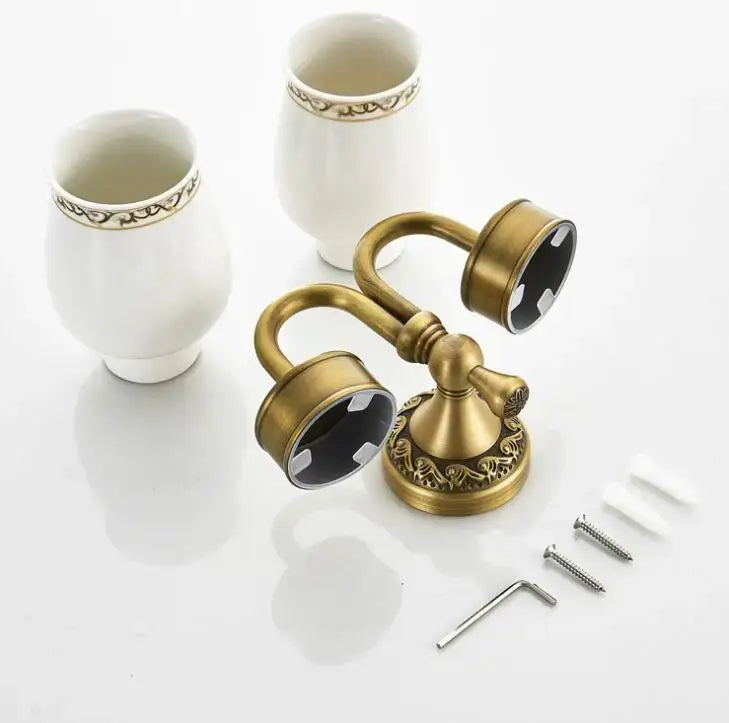 Antique brass double cup holder with ornate scrollwork base and matching decorative cups for bathroom use