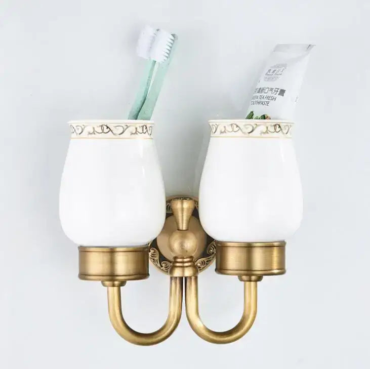 Ornate white ceramic double cup holder with gold-toned metal bracket and decorative rim for bathroom use