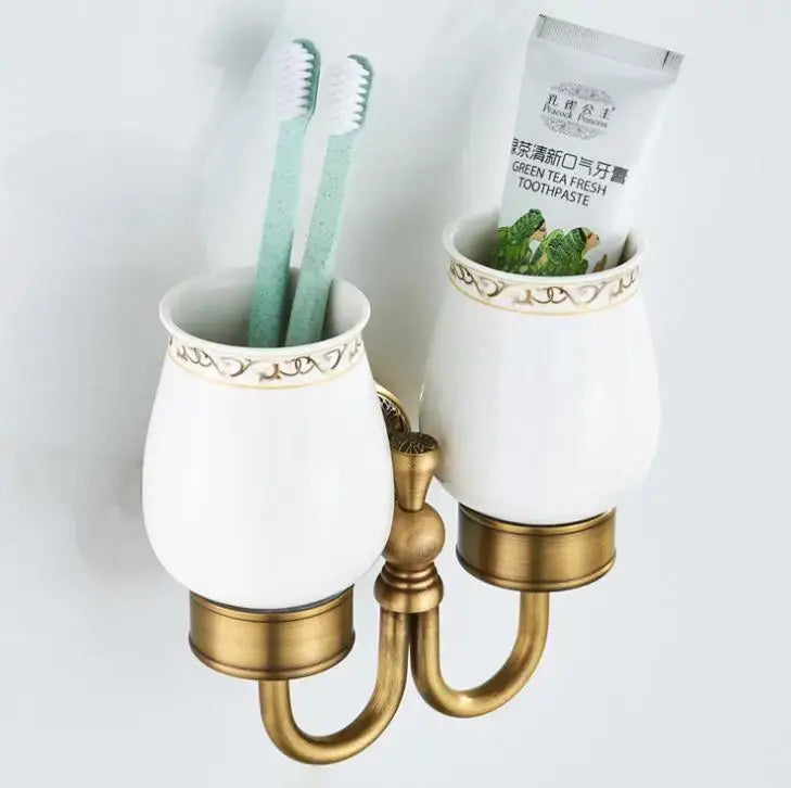 Ornate white ceramic double cup holder with gold-toned metal accents for bathroom toothbrush and toothpaste storage
