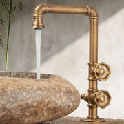Brass industrial-style single hole outdoor antifreeze faucet with ornate gear handles and 360° swivel spout flowing water