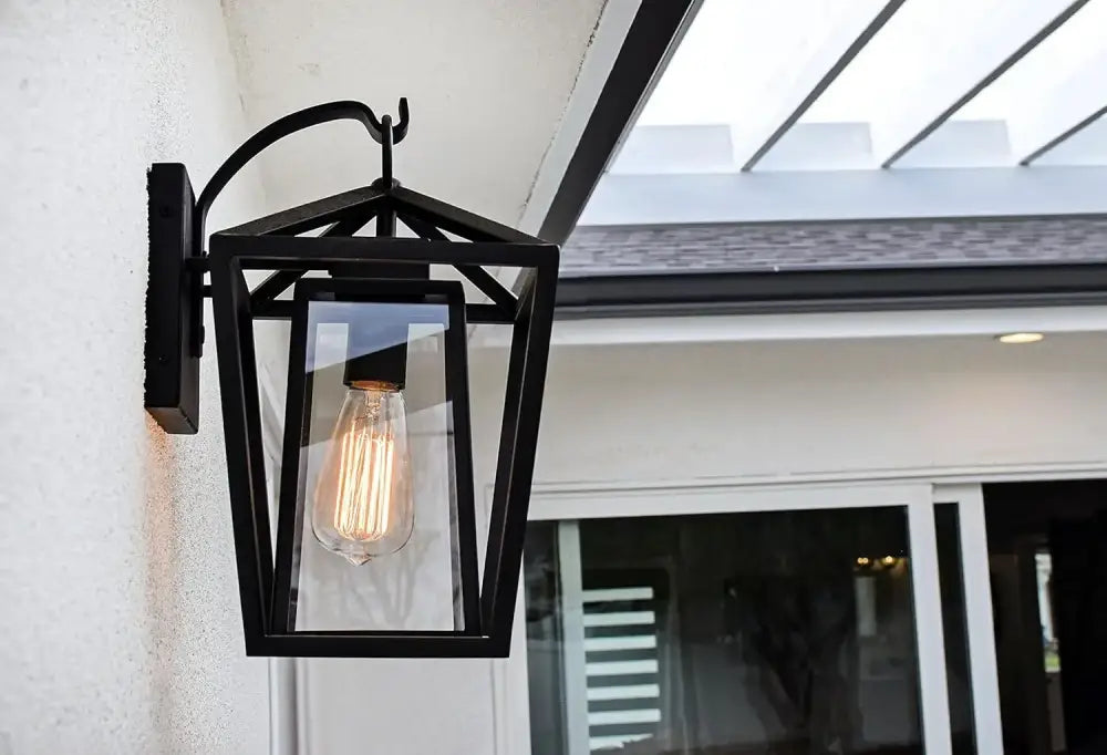Black wrought iron outdoor wall light with glass shades housing glowing filament bulb for waterproof use