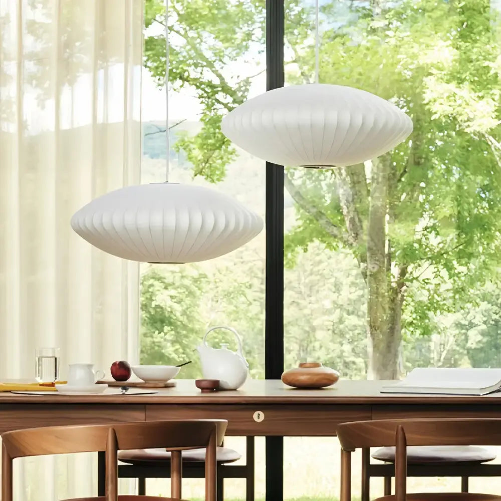 Two white oval ribbed bubble silk pendant chandeliers hang above a wooden dining table for decorbites bubble silk decor
