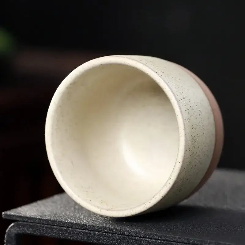 A pastel and terracotta ceramic tea cup set featuring a speckled off-white tea cup with a smooth pink base band