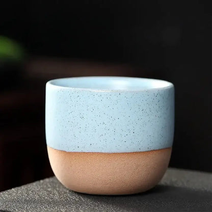 A ceramic tea cup with light blue speckled upper half and earthy tan lower half in a pastel and terracotta cup set