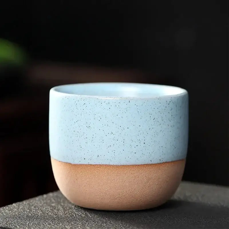 A ceramic tea cup with light blue speckled upper half and earthy tan lower half in a pastel and terracotta cup set