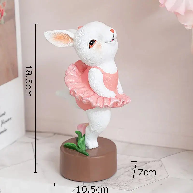 White ceramic ballet rabbit dancer sculpture in pink ruffled leotard on brown base with green leaves for bedroom decor