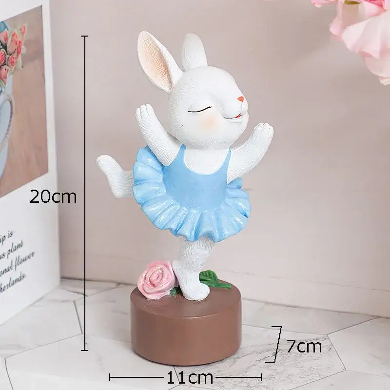 White ceramic ballet rabbit dancer sculpture wearing a light blue tutu on a brown base with a pink rose for bedroom decor