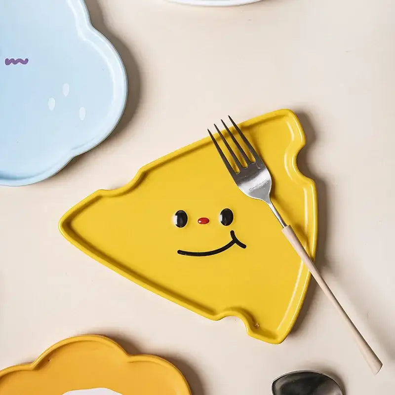 Bright yellow ceramic plate shaped like a cheese slice with smiling face design from decorbites cloud tulip tableware