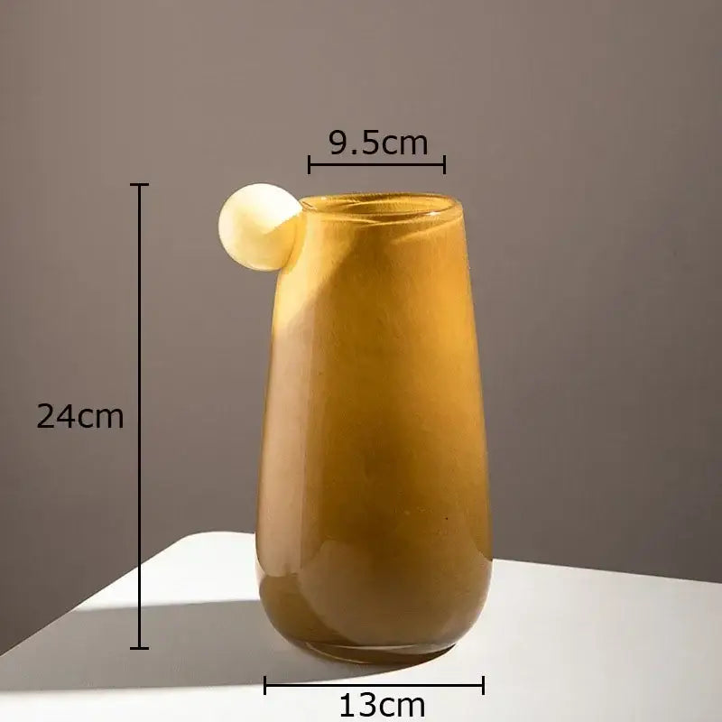 A tall amber colorful glass vase with a smooth tapered design and a small white spherical accent for living room decor