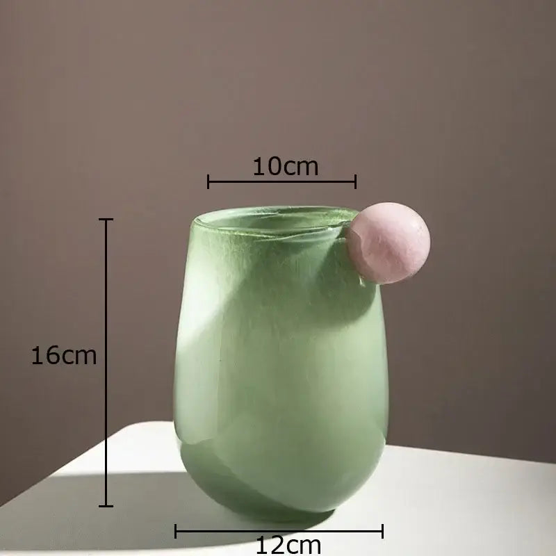 A translucent sage green colorful glass vase with a smooth rounded body and a pink spherical accent for living room decor