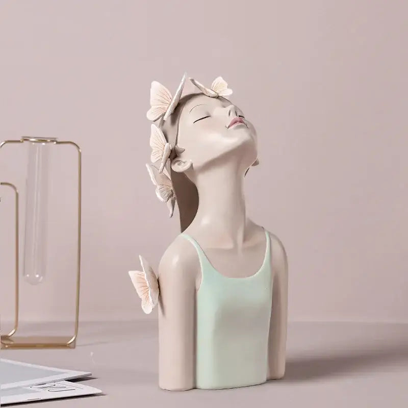 A cream-colored fairy resin figurine with closed eyes and butterflies on hair and shoulder on gold tray decorbites butterfly fairy