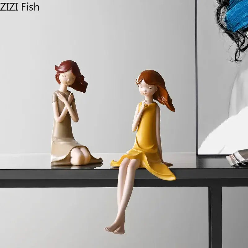Two stylized beige and yellow cartoon girl resin sculptures with flowing hair seated on a shelf decorbites cartoon girl decor
