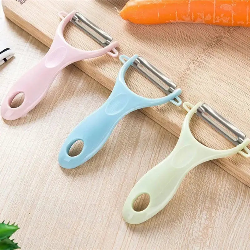 Three pastel decorbites ceramic kitchen peelers with stainless steel blades arranged diagonally on wooden surface