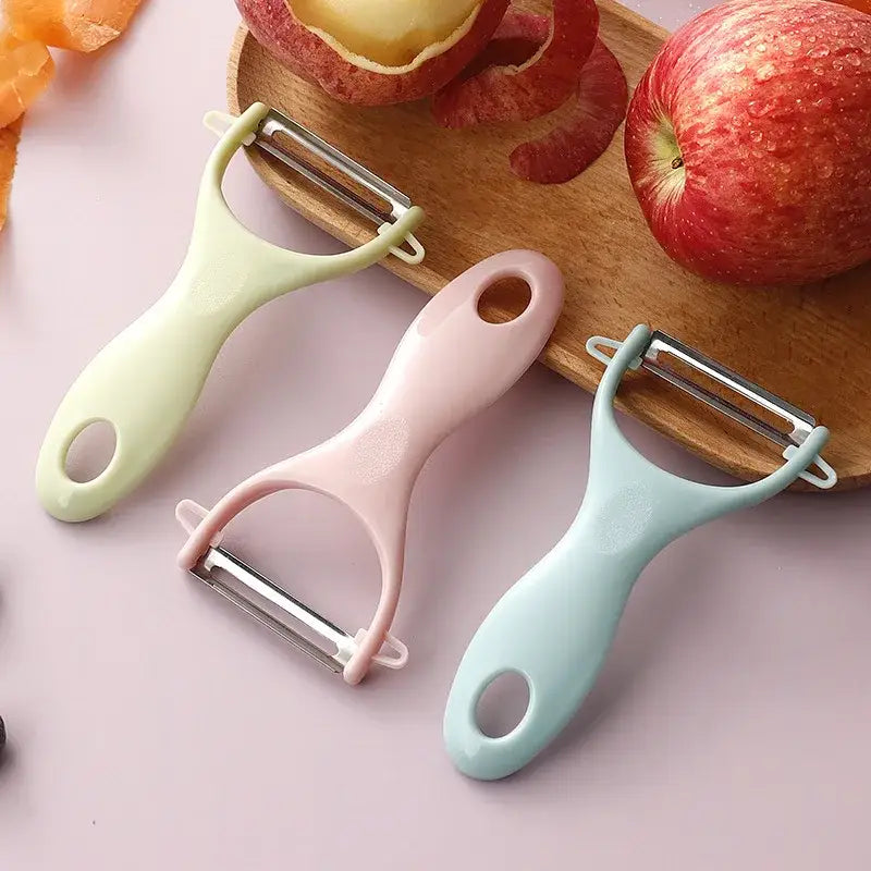 Three pastel ceramic kitchen peelers with stainless steel blades on wooden board beside apples by decorbites ceramic