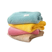 Stack of four pastel corduroy cozy hug blankets in soft blue yellow pink and beige soft sweatshirt throw decorbites cozy hug