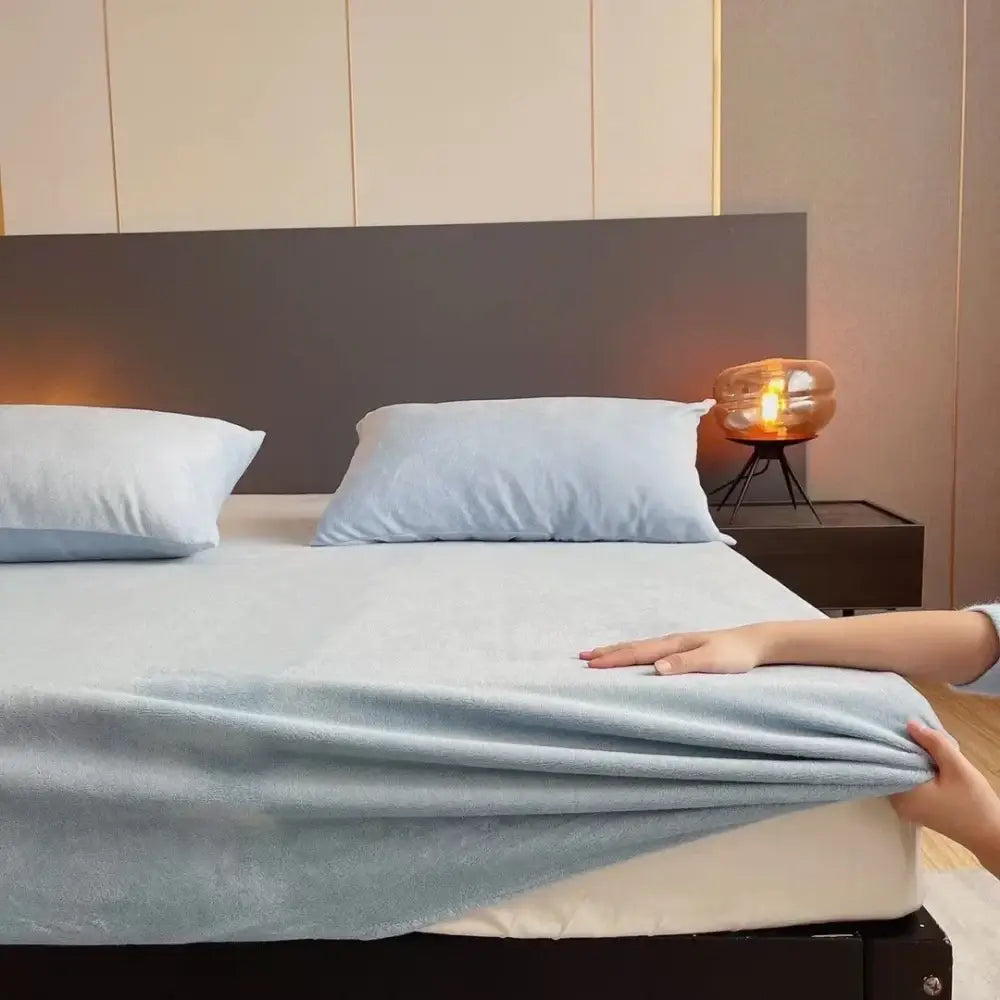 Light blue decorbites cozy flannel queen bed sheet with soft texture being smoothed over a plush mattress cover