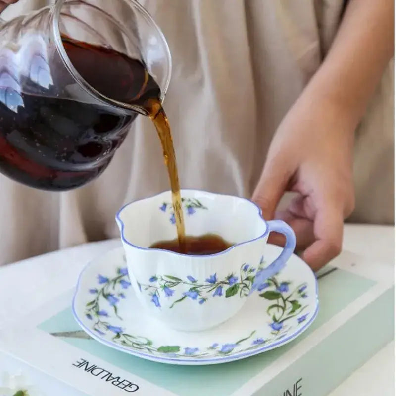 A delicate white porcelain coffee cup and saucer set with scalloped rim and blue floral pattern decorbites bone